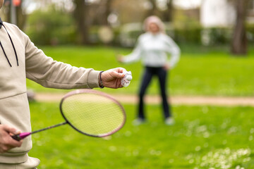Man and woman playing badminton outdoors, focus on hand with shuttlecock