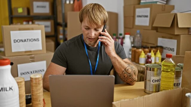 A blond man with a beard coordinates donations indoors while talking on the phone and using a laptop.
