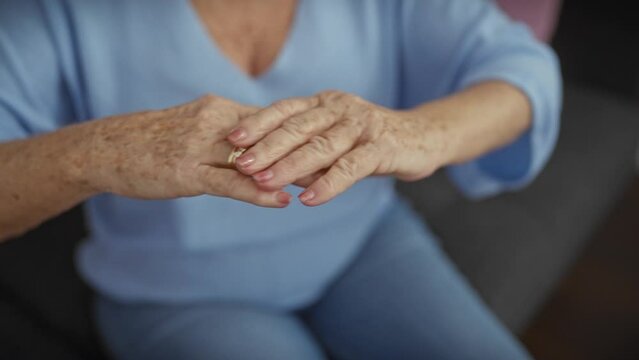 An elderly woman applies lotion to her aging hands indoors, depicting a sense of self-care and the passage of time.