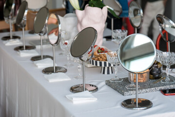 A row of metal table mirrors are lined up on a white tablecloth next to a marble tray, champagne...