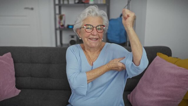 Joyful senior woman flexing arm muscles indoors showcasing strength and vitality.