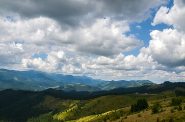 Scenic view of lush green mountains with small wooden shepherds house In the distance under a sky filled with fluffy clouds. Carpathian Mountains, Ukraine
