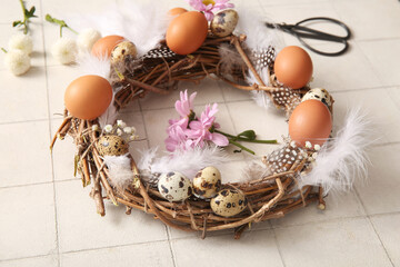 Supplies for creating Easter wreath with eggs, flowers and feathers on white tile background