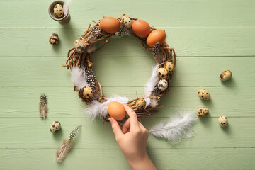 Woman making Easter wreath with eggs and feathers on green wooden background