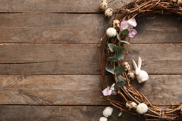 Beautiful Easter wreath with eggs, flowers and plant branches on brown wooden background