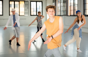 Smiling teenage boy having group dance training in studio, performing dynamic elements