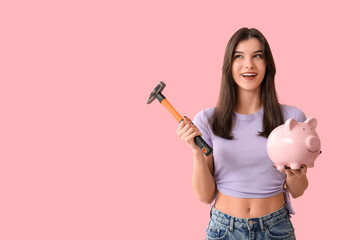 Beautiful young happy woman with piggy bank and hammer on pink background