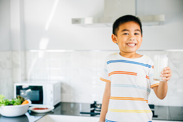 Portrait of happy Asian preschooler, boy holding milk in kitchen. Smiling son enjoys drink,...