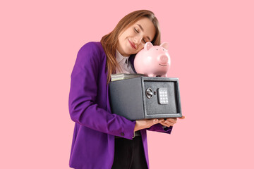 Beautiful young happy woman with safe box, piggy bank and money on pink background