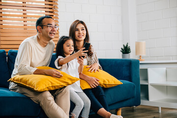Family time is filled with joy and togetherness as an Asian family watches TV movies on the sofa in their grooved modern house. The father mother son and daughter are all smiles.
