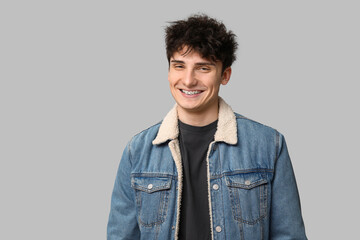 Handsome young man in stylish denim jacket on grey background