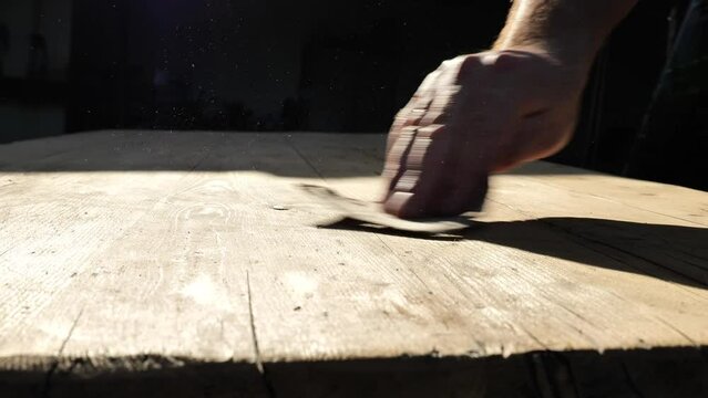 hand sands wooden boards in the suns rays. sanding wood. Processing wood with sandpaper.movement of dust in the suns rays.Wood surface treatment process. 4k footage