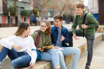 Cheerful teenagers sitting together, talking and having fun outdoors