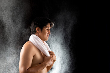 After an intense exercise session, a fit male athlete pauses to wrap a towel around his neck,...