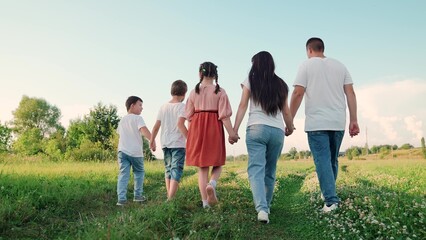 Family walks through meadow holding hands. Dad mom son daughter. Happy family with children walks in city park in summer. Parents children go together, family weekend. Mom, dad, child, big family. - obrazy, fototapety, plakaty