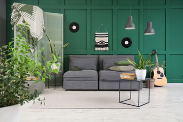 Beautiful interior of green living room with cozy black sofa, coffee table and houseplants
