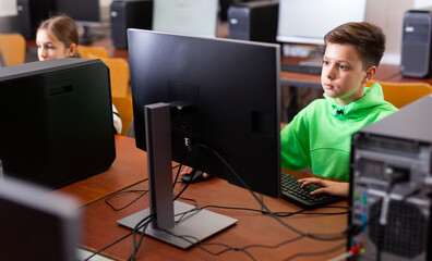 Smart focused tween boy studying with classmates in modern computer lab at school..