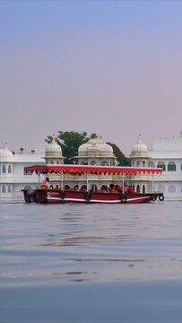 Famous luxury Udaipur Lake Palace Jag Niwas on island on lake Pichola on sunsets. Tourist boat is heading to the side. Udaipur, Rajasthan, India. Camera pan