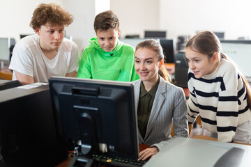 Fototapeta premium Female teacher and her students, young girl and boys, looking at monitor of PC during computer science lesson.