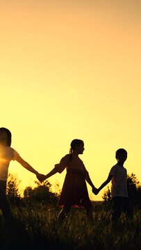 Big family walks across field holding hands against sunset. Happy parents, children silhouettes go in meadow joining hands at setting sun. Family travels in countryside spending time together. Kids
