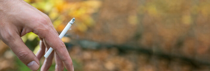 close-up of man's hand holding cigarette, autumn background