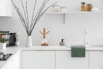 Vase with willow branches on counter in interior of light kitchen - obrazy, fototapety, plakaty