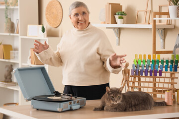 Senior woman with cute cat and record player listening to music at home