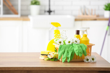 Basket with set of cleaning supplies and spring flowers on wooden table in kitchen