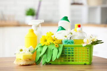 Basket with set of cleaning supplies and spring flowers on wooden table in kitchen