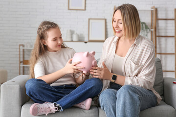 Mother and her daughter holding piggy bank at home. Education savings concept