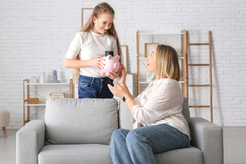 Mother and her daughter holding piggy bank with mortar board at home. Education savings concept
