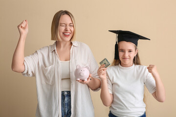 Happy mother and her daughter in mortar board holding piggy bank and money on beige background....