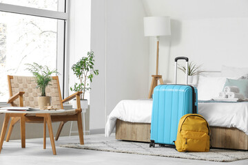 Interior of light hotel room with suitcase and backpack near bed