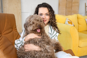 Young woman with cute poodle sitting in armchair at home