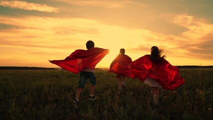 Child imagine being comic book heroes running across meadow in red capes. Children in red capes run...