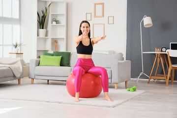 Sporty young woman exercising on fitness ball at home