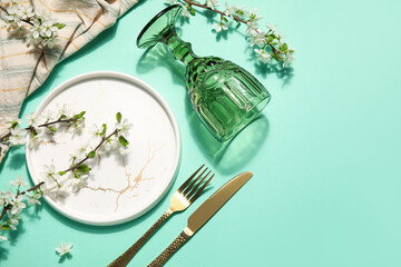 Beautiful table setting with golden cutlery and blossoming branches on turquoise background