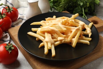 Delicious French fries with cheese sauce, tomatoes, dill and parsley on grey table, closeup