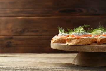 Tasty canapes with salmon, cucumber, cream cheese and dill on wooden table, space for text
