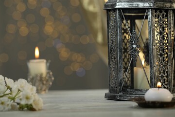 Arabic lantern and burning candles on table against blurred lights
