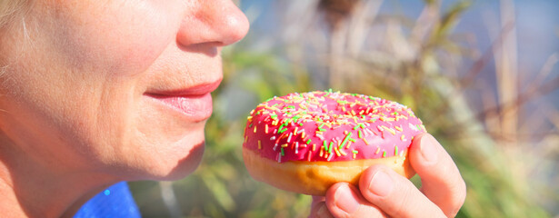 Senior woman eating pink doughnut. Sweet food. Banner