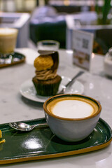 Taza de café con leche en primer plano en mesa de bar con bombón de chocolate desenfocado al fondo. Desayunos y meriendas