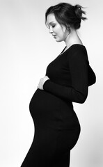 Black and white portrait of pregnant female in black dress with hands near pregnant belly. - 787710514