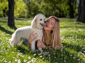 Cute blonde girl laying on the grass with her pet poodle , spring time 
