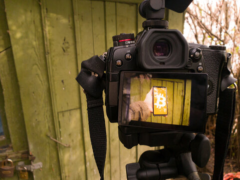 On the display of a digital camera, a hand-held smartphone displaying a bitcoin symbol. BTC concept, a green wooded forest house with nature in the background.