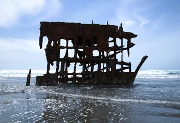 Metal frame of a ship washed up on the shore, a part of the Peter Iredale Shipwreck, with waves splashing over them on a clear sunny day.  © Katherine