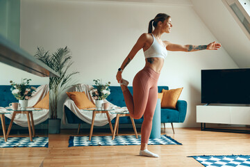 Smiling woman is stretching her thigh in living room for fun and leisure. Healthy lifestyle concept