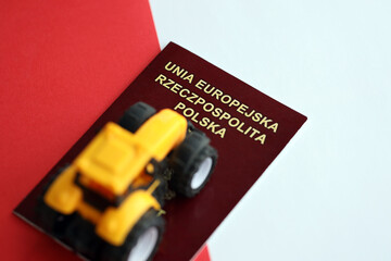 Red polish passport and yellow tractor on smooth red and white flag of Poland close up