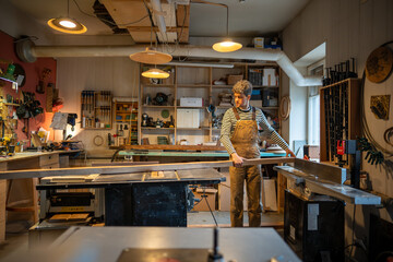 Carpentry workshop, craftsman master working with circular saw. Guy on workplace with large...