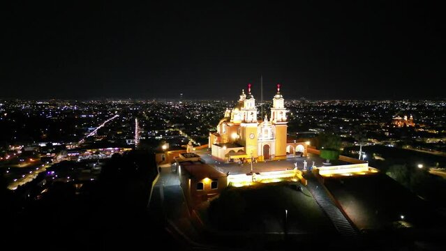 Video a&eacute;reo circular de la Iglesia de Cholula, Puebla de noche. Se pueden ver las luces de la ciudad de Puebla en lo bajo de la iglesia.